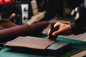 male artisan carefully punching piece of leather at professional leather workshop