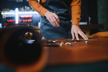 Production process. Young focused experienced master craftsman makes leather goods at his workplace