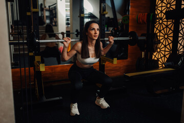 Determined sportswoman performing squats with barbell in modern gym