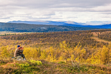Man sitting and looking through binoculars in a mountain landscape in autumn
