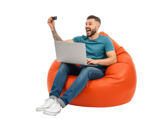 Excited tattooed man on beanbag chair holding credit card and using laptop isolated transparent