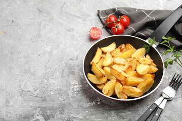 Tasty baked potatoes in frying pan, forks, parsley and tomatoes on grey textured table. Space for text