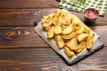 Tasty baked potatoes with rosemary and ketchup on wooden table. Space for text