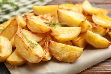 Tasty baked potatoes with rosemary on wooden table, closeup