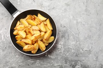 Tasty baked potatoes in frying pan on grey textured table, top view. Space for text