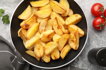 Tasty baked potatoes in frying pan, tomatoes and spices on grey textured table, flat lay