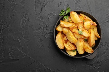 Tasty baked potatoes with parsley in frying pan on dark textured table, top view. Space for text