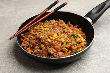 Delicious fried rice with vegetables in frying pan and chopsticks on grey textured table, closeup
