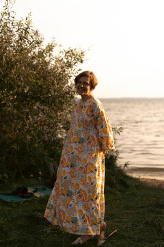 Smiling woman in a colorful dress standing by the lakeside at sunset