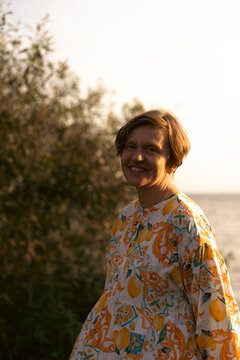Smiling woman in a colorful dress standing by the lakeside at sunset