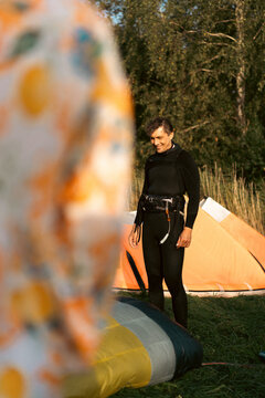 Smiling man in wetsuit standing next to kite, ready for kite surfing