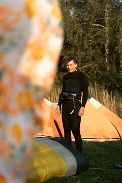 Smiling man in wetsuit standing next to kite, ready for kite surfing