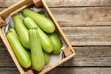 Fresh ripe zucchinis in crate on wooden table, top view. Space for text