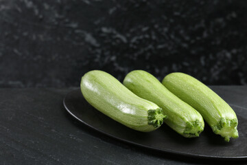 Fresh ripe zucchinis on black textured table, closeup. Space for text