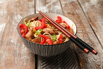 Delicious noodles with meat, vegetables and chopsticks on wooden table, closeup