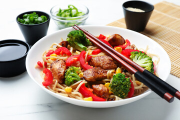 Delicious noodles with meat and vegetables served on white marble table, closeup