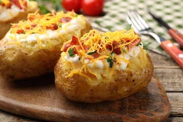 Tasty baked potatoes with sour cream, green onion, cheese and bacon on wooden table, closeup