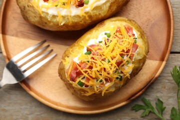 Tasty baked potatoes with sour cream, green onion, cheese and bacon served on wooden table, flat lay