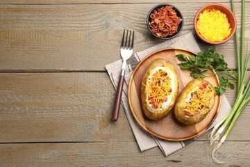 Tasty baked potatoes with sour cream, green onion, cheese and bacon served on wooden table, flat lay. Space for text