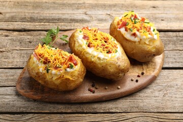 Tasty baked potatoes with sour cream, green onion, cheese, bacon and peppercorns on wooden table, closeup