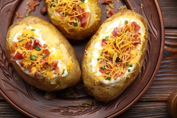Tasty baked potatoes with sour cream, green onion, cheese and bacon on wooden table, top view