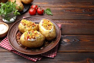 Tasty baked potatoes with sour cream, green onion, cheese and bacon on wooden table. Space for text