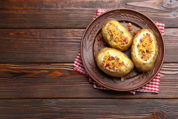 Tasty baked potatoes with sour cream, green onion, cheese and bacon on wooden table, top view. Space for text