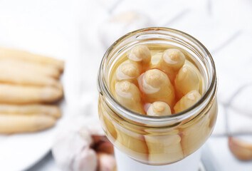 Pickled asparagus in jar on white table, closeup
