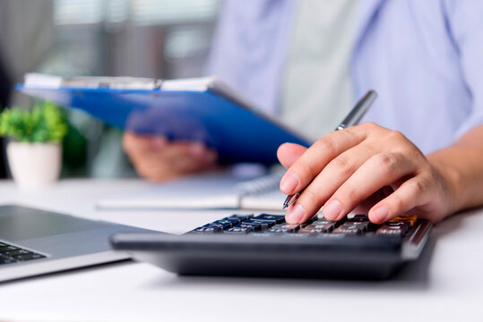 Accountant presses calculator with pen laptop and clipboard on office desk calculate budget, verify numbers, and prepare financial report. close-up hands accuracy, audit, and productivity concept.