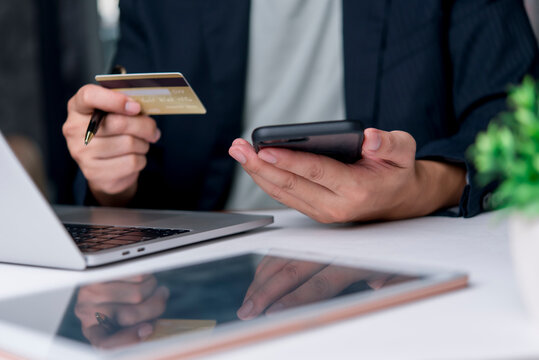 Business user pays with credit card via smartphone at office desk near laptop tablet, mobile payment online banking finance transaction security convenience concept.