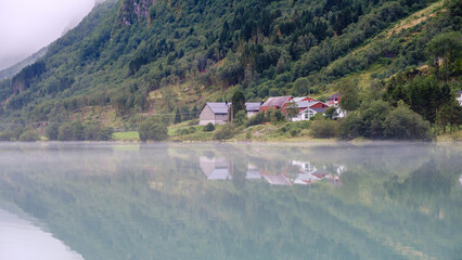 Nestled between lush mountains, the quiet village by Bergheimsvatnet showcases charming Norwegian architecture. Mist hangs gently over the calm water, creating a mirror-like effect at dawn.
