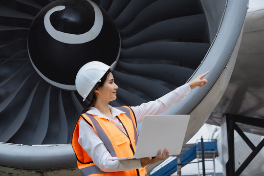 An Asian woman stands confidently in front of a jet engine,wearing a safety helmet  reflective vest,holding tablet,representing aviation engineering,safety inspection,professional roles in airline