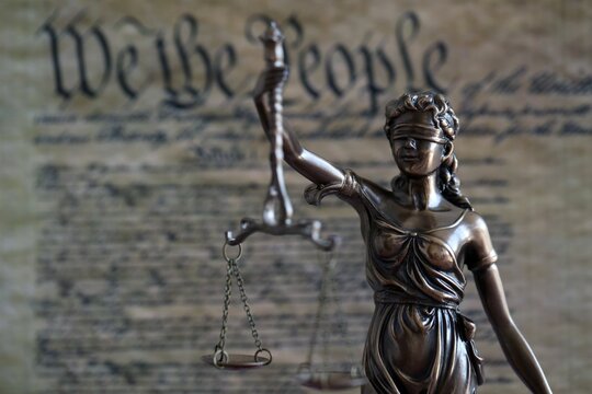 Dark scene with Lady Justice and background of blurred US Constitution page - Powered by Adobe