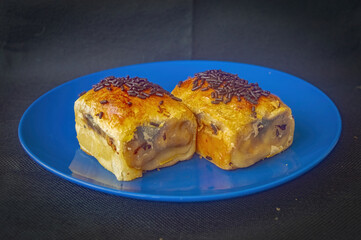 Two pieces of Indonesian bolen pastry with fruit fill and chocolate sprinkles on blue plate showcasing golden crust, sweet layers, and artisanal texture for bakery and culinary visuals.