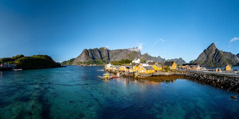 Brightly painted cabins line the tranquil waters of Sakrisoy, Lofoten, Norway, under a clear blue sky. © Fokke Baarssen