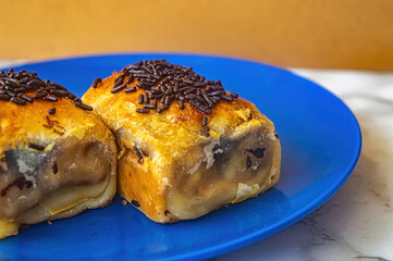 Two pieces of Indonesian bolen pastry with golden crust, dark fill, and chocolate sprinkles on blue plate highlighting sweet layers, baked texture, and local dessert appeal for food styling.