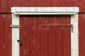 A red barn door features peeling paint and hardware, showcasing a rustic countryside aesthetic that evokes a sense of nostalgia.