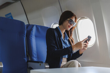 Businesswoman using smartphone on airplane near window