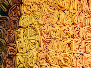 A stack of colorful hijabs or headscarves neatly folded into a square roll. A head covering for Muslim women.