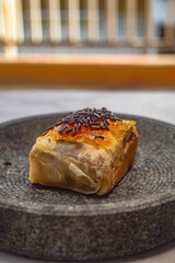 Golden puff pastry roll with flaky crust and creamy filling, topped with chocolate sprinkles on dark plate ideal for showcasing baked texture, sweet detail, and snack appeal.