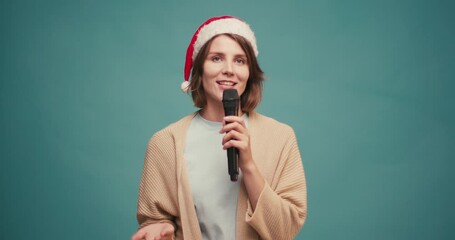 Friendly Hispanic woman in red santa hat with mic makes Christmas announcement and happy smiling on blue background - Powered by Adobe