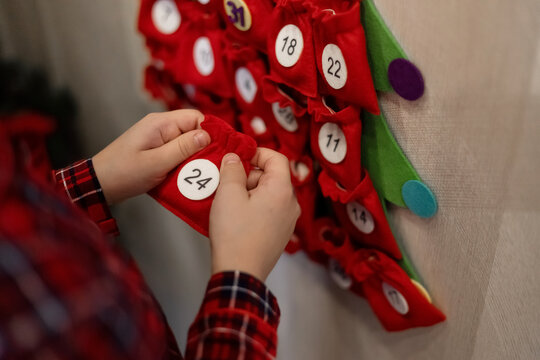 Closeup hands of a young boy wearing Christmas pajamas and a Santa Claus hat looking for a surprise in the advent calendar at home. December 24 on the calendar