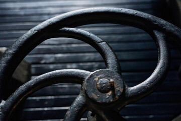 Worn-down black industrial control wheel on an old gas-powered engine, part of a vintage machinery display in an industrial museum