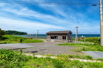 海辺にたたずむ小さな無人駅舎と日本海の風景。駅舎の看板には漢字で”とどろきえき”と記されている。