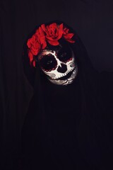 Close up portrait of a woman wearing la Catrina makeup and red roses on her head, black background 