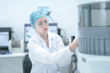 A medical scientist wearing protective equipment prepares an automated analyzer by inserting a patient sample tray to begin the biological testing process in a hospital laboratory.