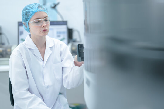 A medical scientist wearing protective equipment prepares an automated analyzer by inserting a patient sample tray to begin the biological testing process in a hospital laboratory.