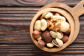 Mix of different nuts in bowl on wooden table, top view. Space for text