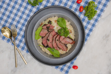 Gourmet Dish: An artistic overhead view of an elegantly plated gourmet dish, presenting perfectly cooked meat atop a bed of meticulously arranged grains and vibrant fresh garnishes.