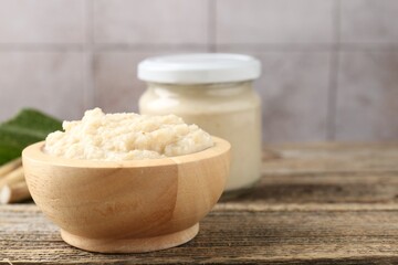Tasty horseradish sauce and roots on wooden table, closeup. Space for text